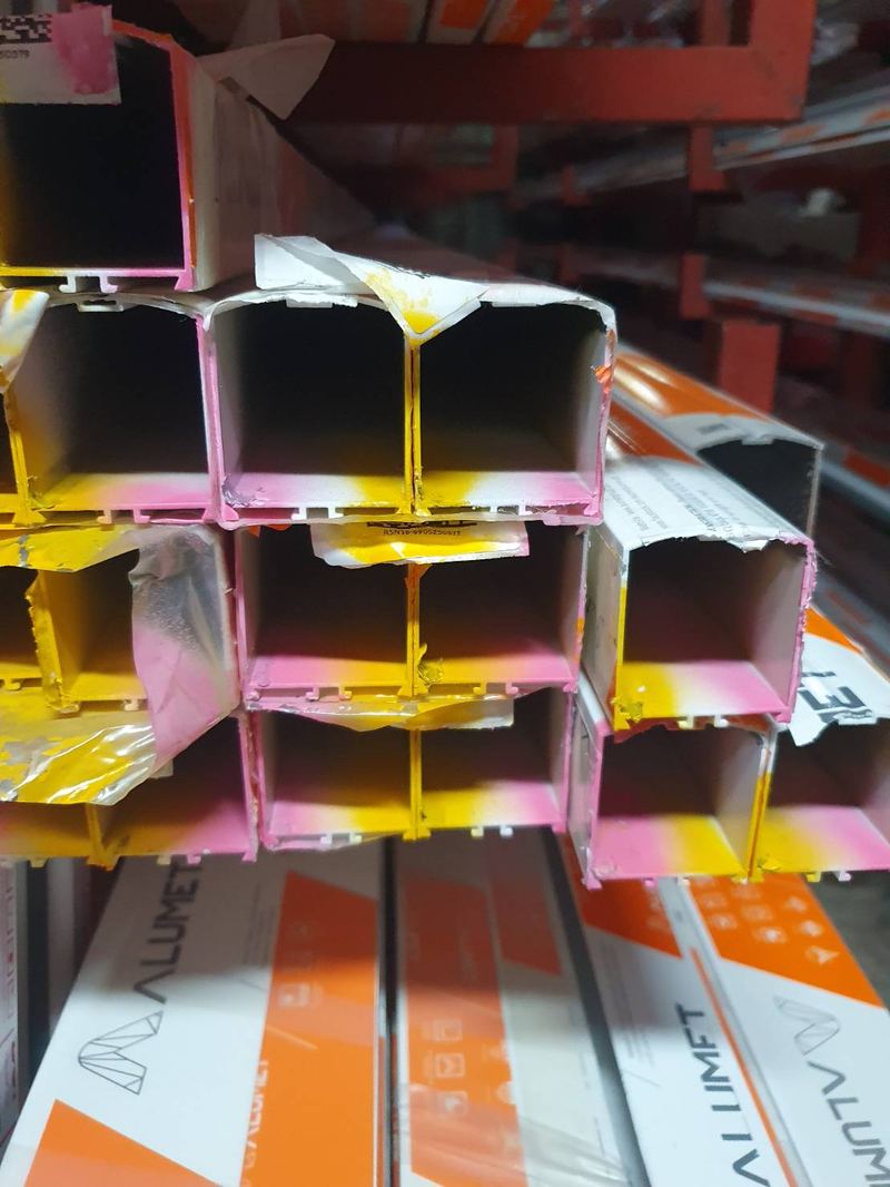 ปลายเส้นเสาประตูสวิงอลูมิเนียม วางซ้อนกันบนชั้นในร้าน เห็นรูปหน้าตัด