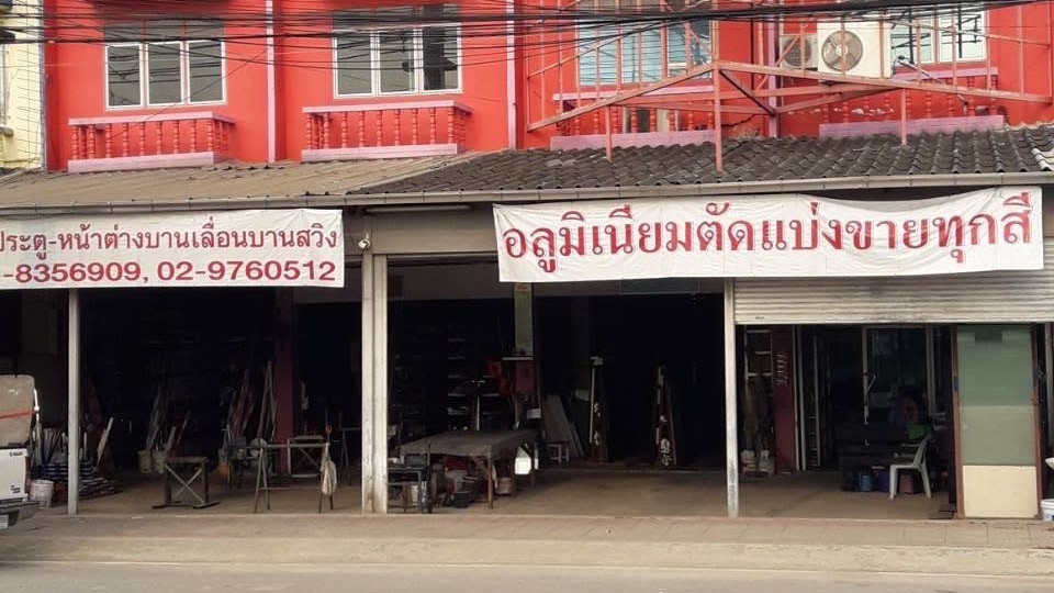 หน้าร้าน หจก.วี อลูมิเนียม ริมถนนใน ต.บางเดื่อ อ.เมืองปทุมธานี ป้ายเขียนว่าอลูมิเนียมตัดแบ่งขายทุกสี