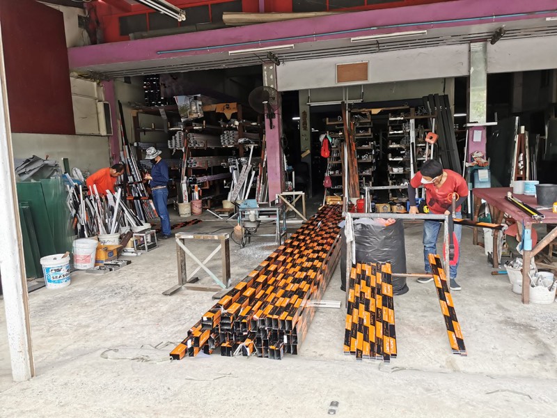 ในร้าน หจก.วี อลูมิเนียม มีโต๊ะตัดและเส้นอลูมิเนียมสีส้มวางเรียงอยู่